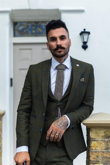 Man in a tailored suit leaning against a stone wall, with a stylish background.