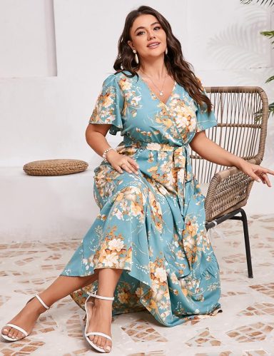 Woman in a floral dress sitting elegantly beside a chair.